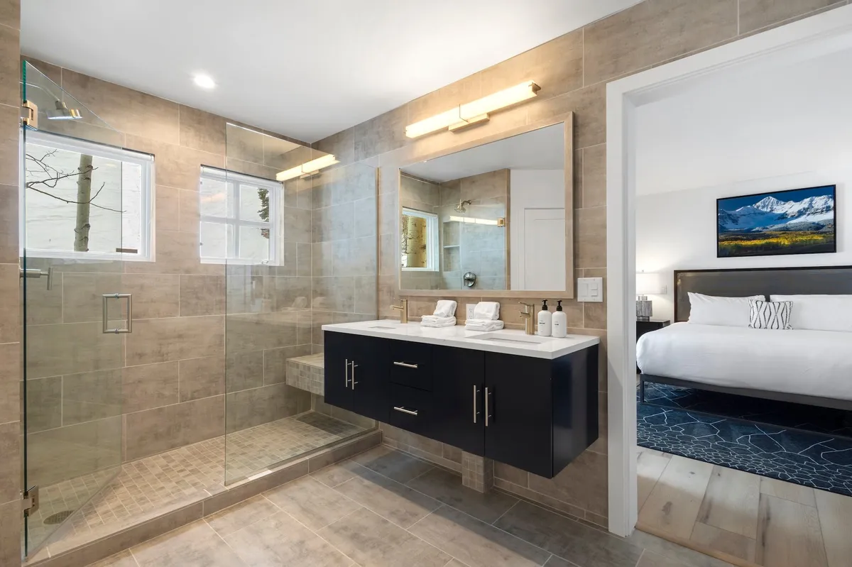 This modern bathroom features a glass-enclosed shower, double vanity with dark cabinetry, expansive mirrors, and ample natural light streaming through windows. The space feels fresh, luxurious, and conducive to relaxation and rejuvenation.