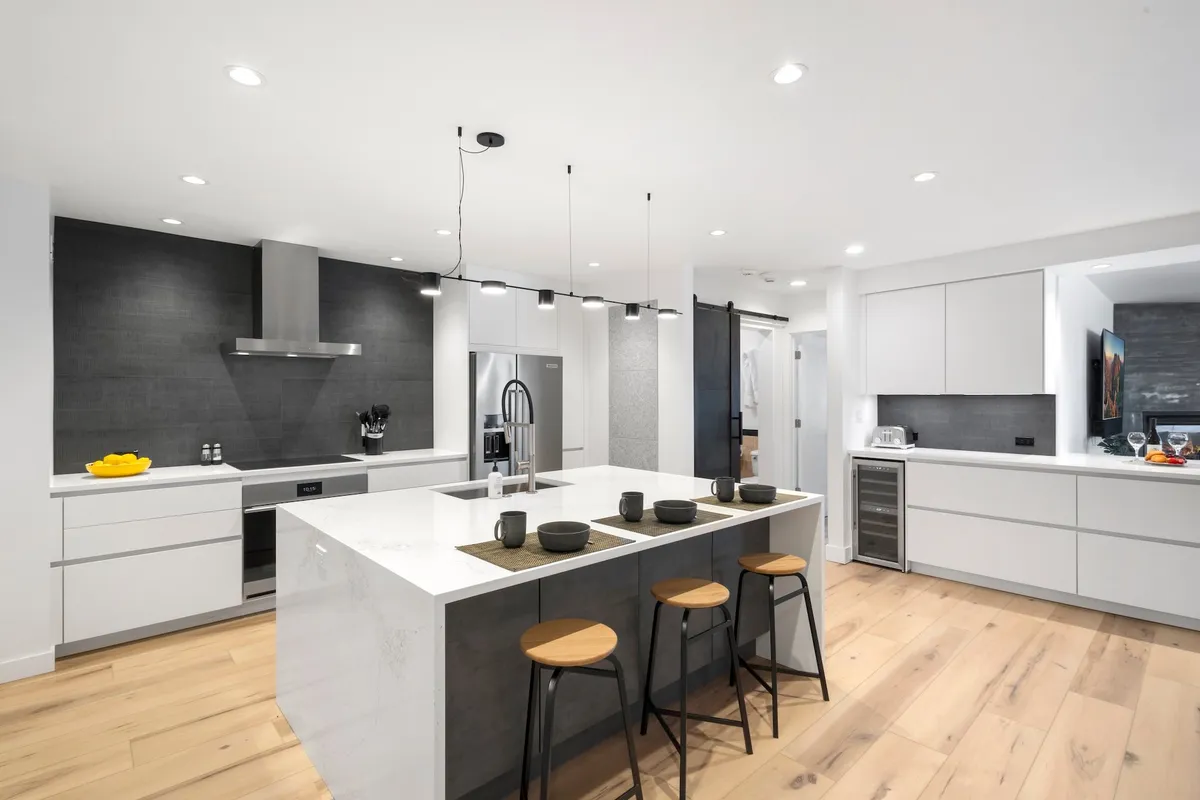 An inviting open-concept kitchen with a large island, stools for casual dining, white cabinetry, and a stylish gray backsplash. The space is designed for both cooking and entertaining, with room for guests to gather around the island.