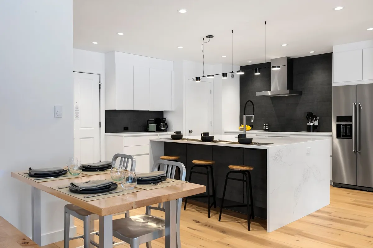 A bright and contemporary kitchen scene featuring a central island with seating, a dining table set for a meal, and sleek cabinetry. The layout invites both cooking and social gatherings, with plenty of space for movement and connection.
