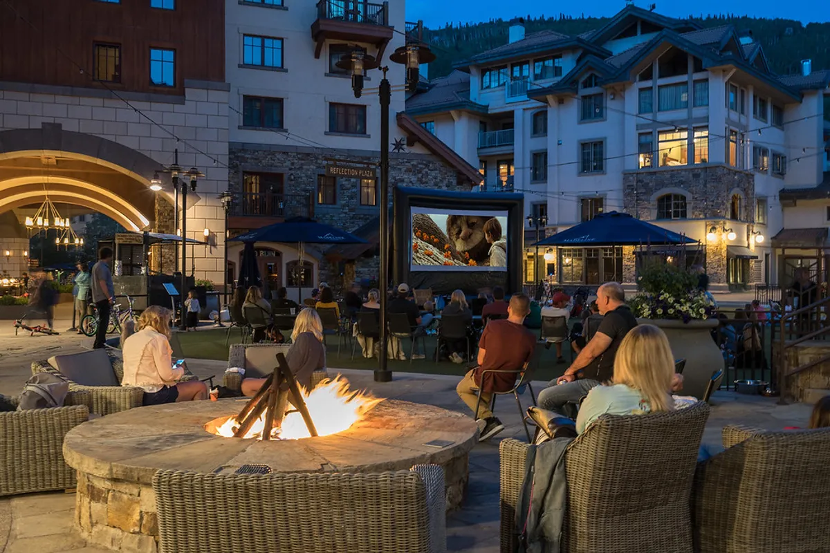 A lively outdoor scene with guests gathered around a glowing fire pit and an outdoor movie screen, evoking memorable evenings spent socializing and relaxing under the stars.