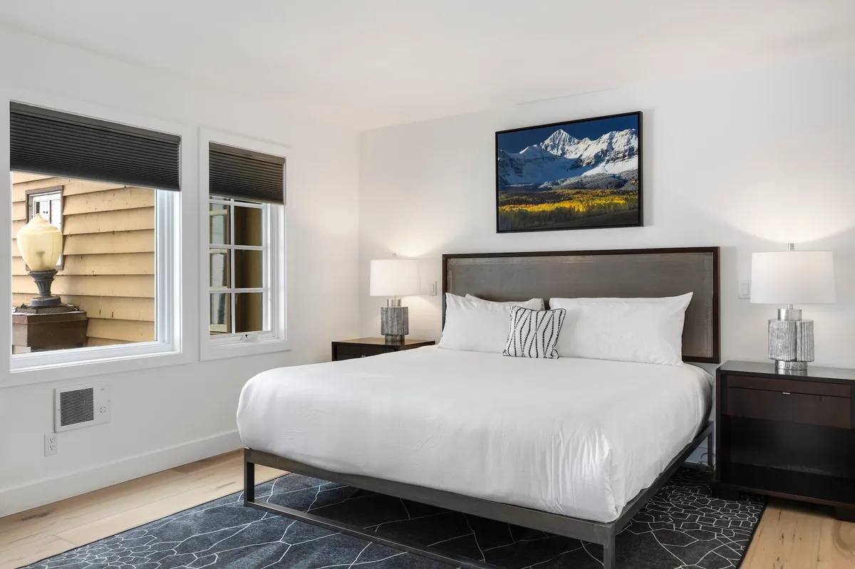 This image shows a tranquil bedroom with a comfortable bed, mountain landscape painting above the headboard, matching nightstands, and softly glowing lamps. The room exudes calm and offers a cozy, restful atmosphere perfect for unwinding after an adventure-filled day.