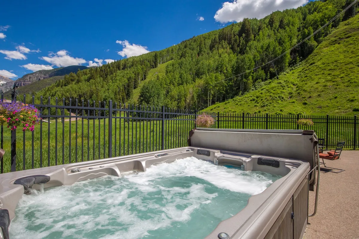 This image presents a close-up exterior shot of a hot tub with a direct mountain view, contained within a private fenced yard. The scene is peaceful and inviting, suggesting both privacy and an immersive mountain experience.