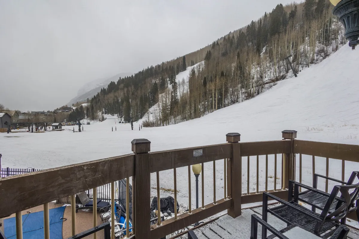An inviting deck overlooks a snow-blanketed landscape with a mountain backdrop, captured in serene winter light. The deck's railing frames the scene, suggesting a cozy vantage point to enjoy outdoor beauty after a day on the slopes.