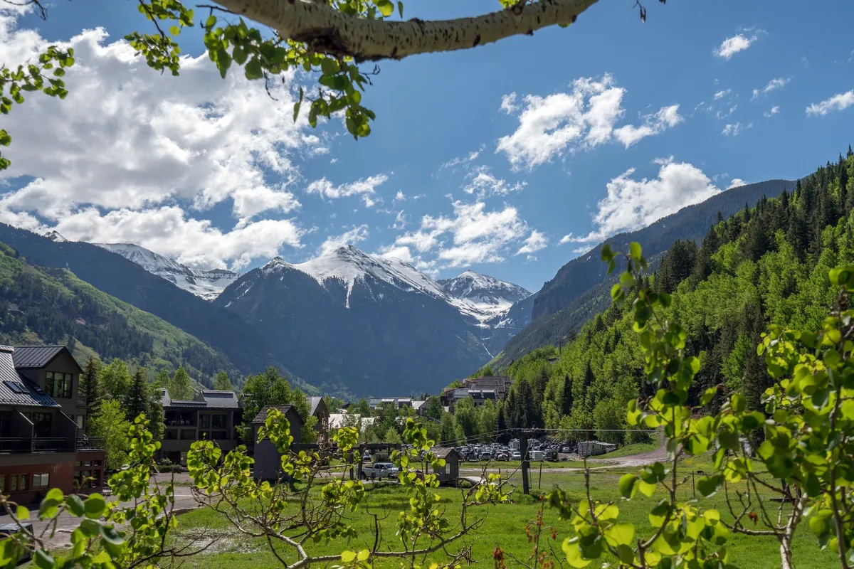 Snow-capped mountains rise behind lush green trees and a vibrant blue sky, capturing the breathtaking natural surroundings guests can explore or admire from the property.