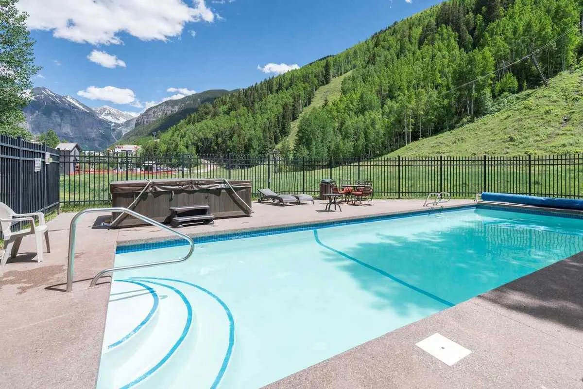 This image features the complex’s swimming pool and hot tub, nestled against a stunning mountain backdrop, with lounge chairs arranged for relaxation. The pool area is inviting, with plenty of space to unwind after a day of outdoor adventure. Both winter and summer amenities are visible, suggesting year-round enjoyment.